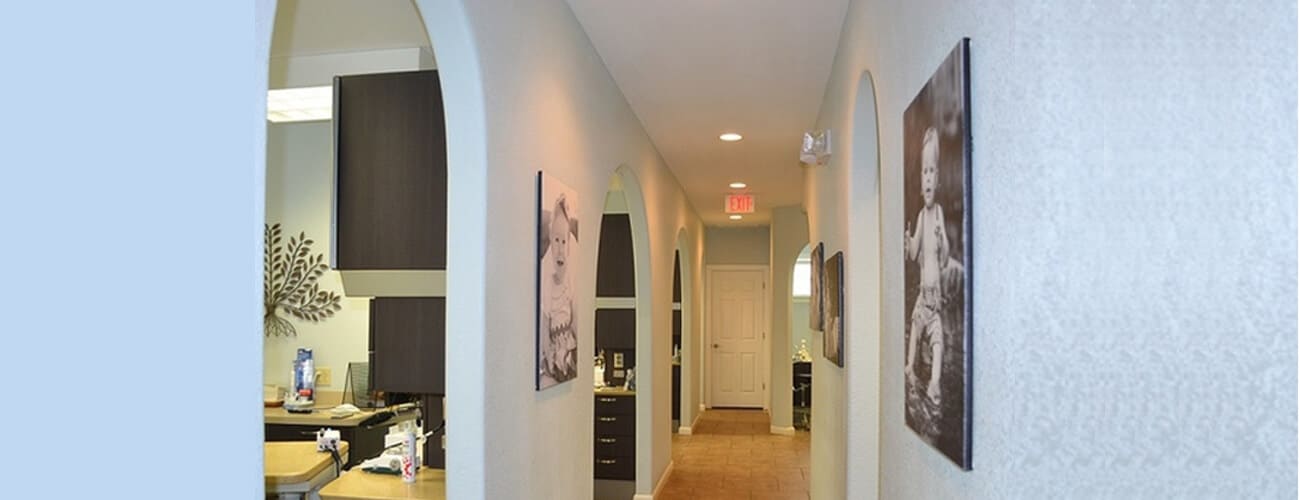 Modern dental office hallway with white walls, framed artwork, and warm lighting throughout corridor.