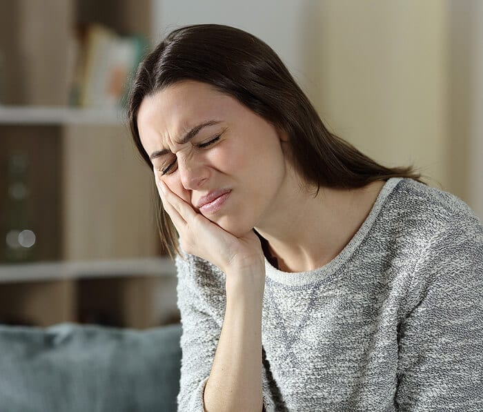 Woman smiling thoughtfully while touching her face in a home living room setting.