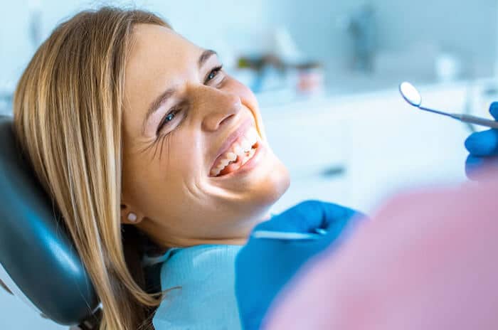 Smiling woman in dental chair wearing blue bib during routine dental examination at clinic.