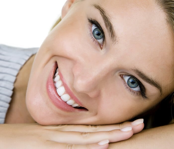 Woman smiling brightly, displaying healthy teeth and fresh complexion against white background.