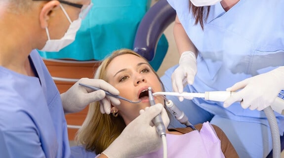 Patient receiving dental examination from dentist and assistant in clinical office setting.
