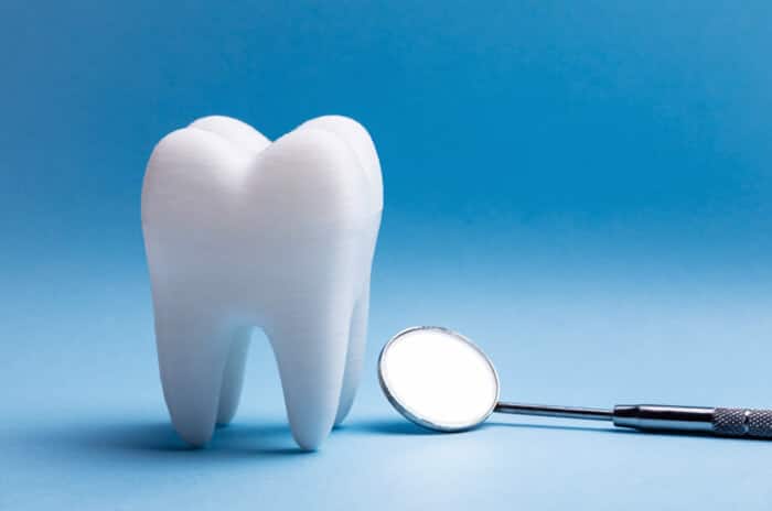 White tooth model next to dental mirror on blue background, representing dental care and examination.