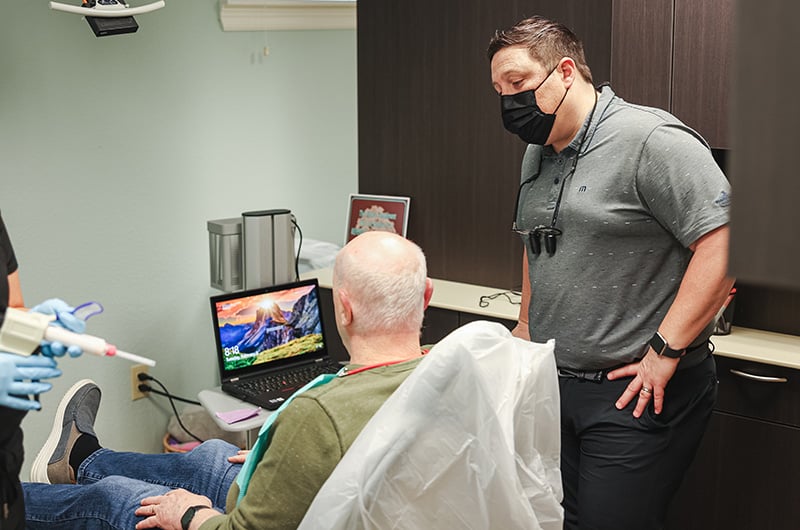 Dental professional explaining treatment plan to seated patient in modern dental office setting.