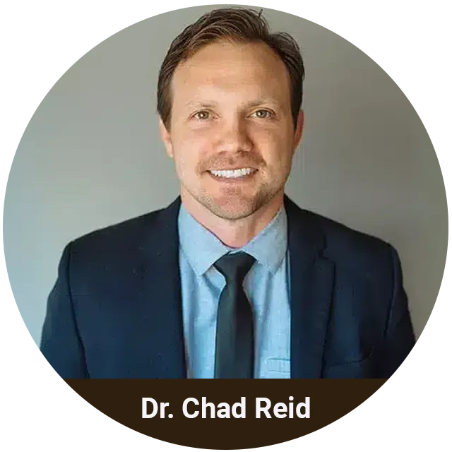 Dr. Chad Reid, dentist, professional headshot wearing navy blazer and blue tie against gray background.